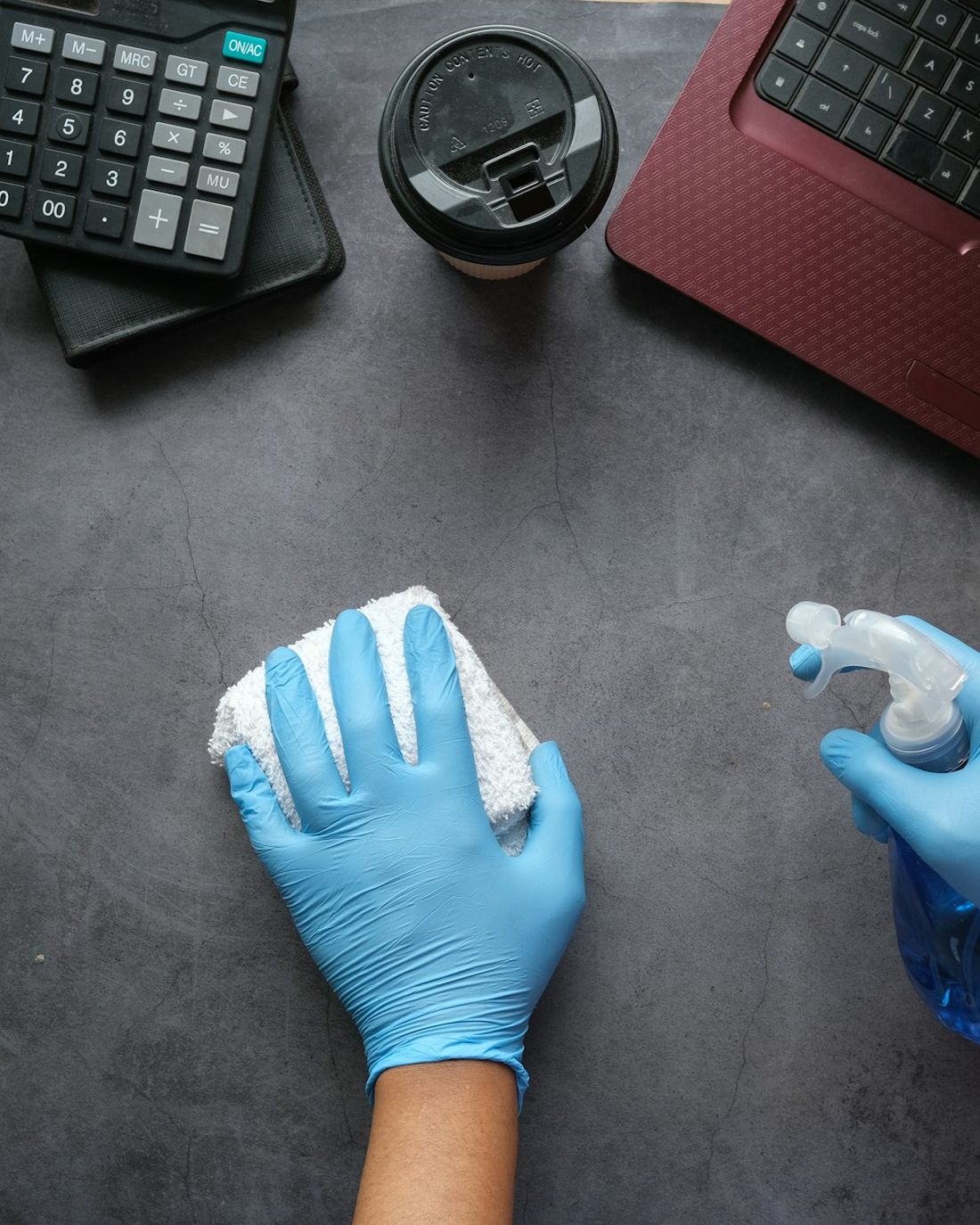 Gloved hands cleaning a desk with a spray bottle